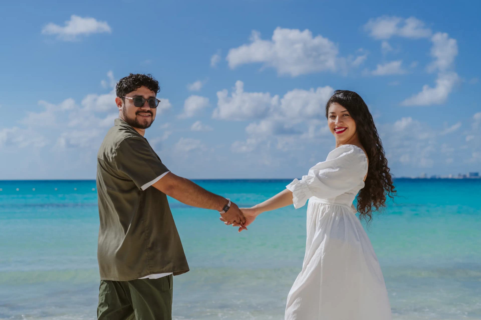 Couple laughing and running on white sand beach during couple photoshoot in Cancun