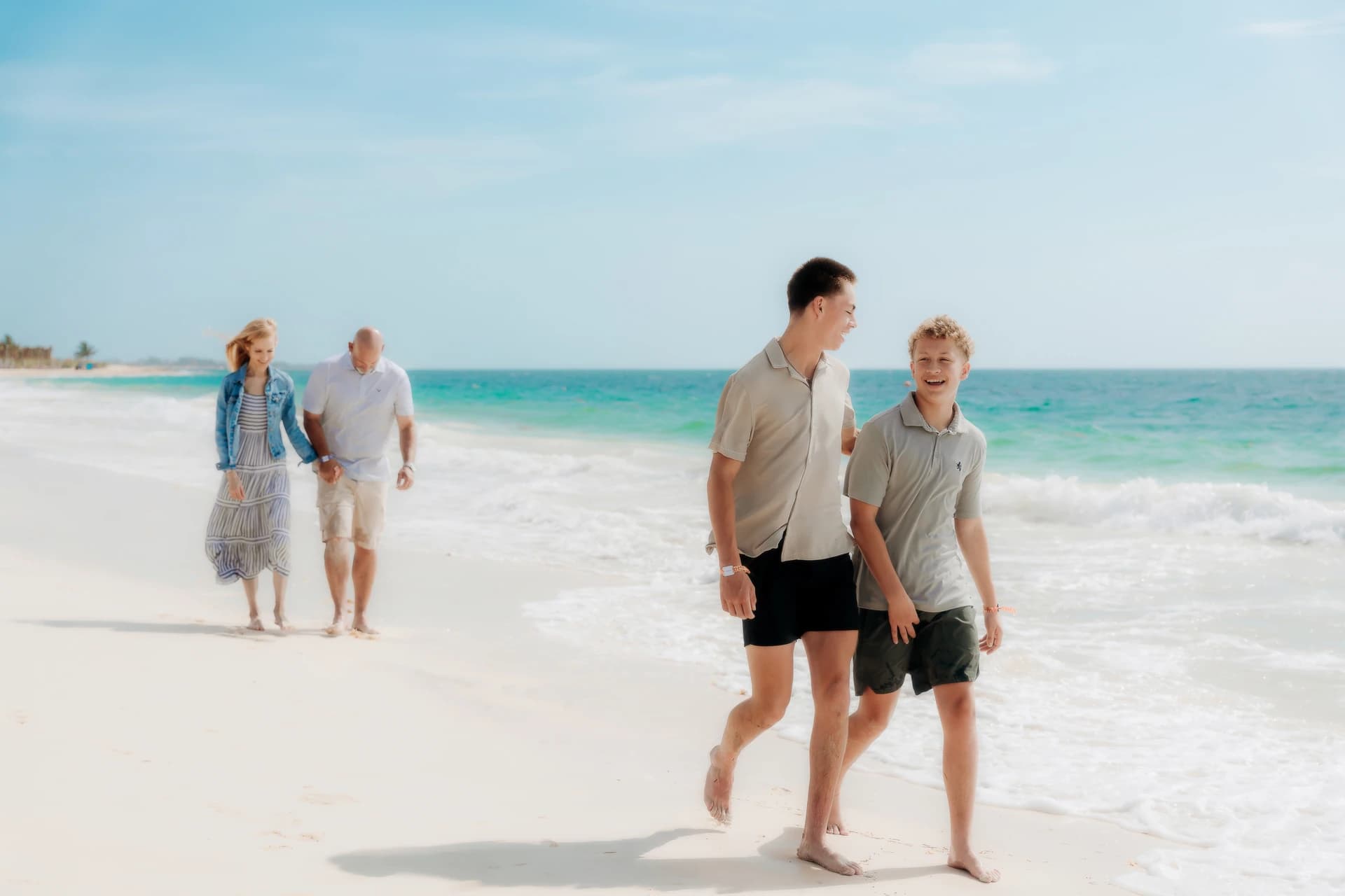 Two brothers walking ahead of their parents along the turquoise Cancún shoreline.