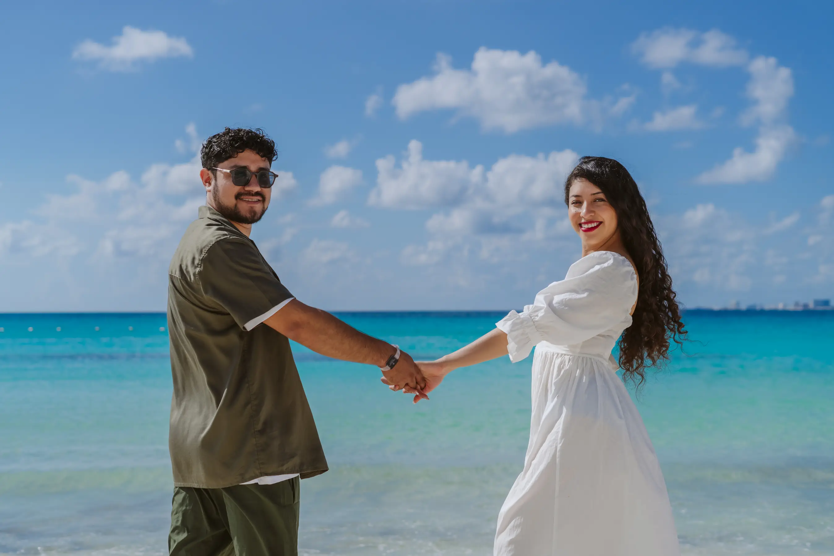 Couple laughing and running on white sand beach during couple photoshoot in Cancun