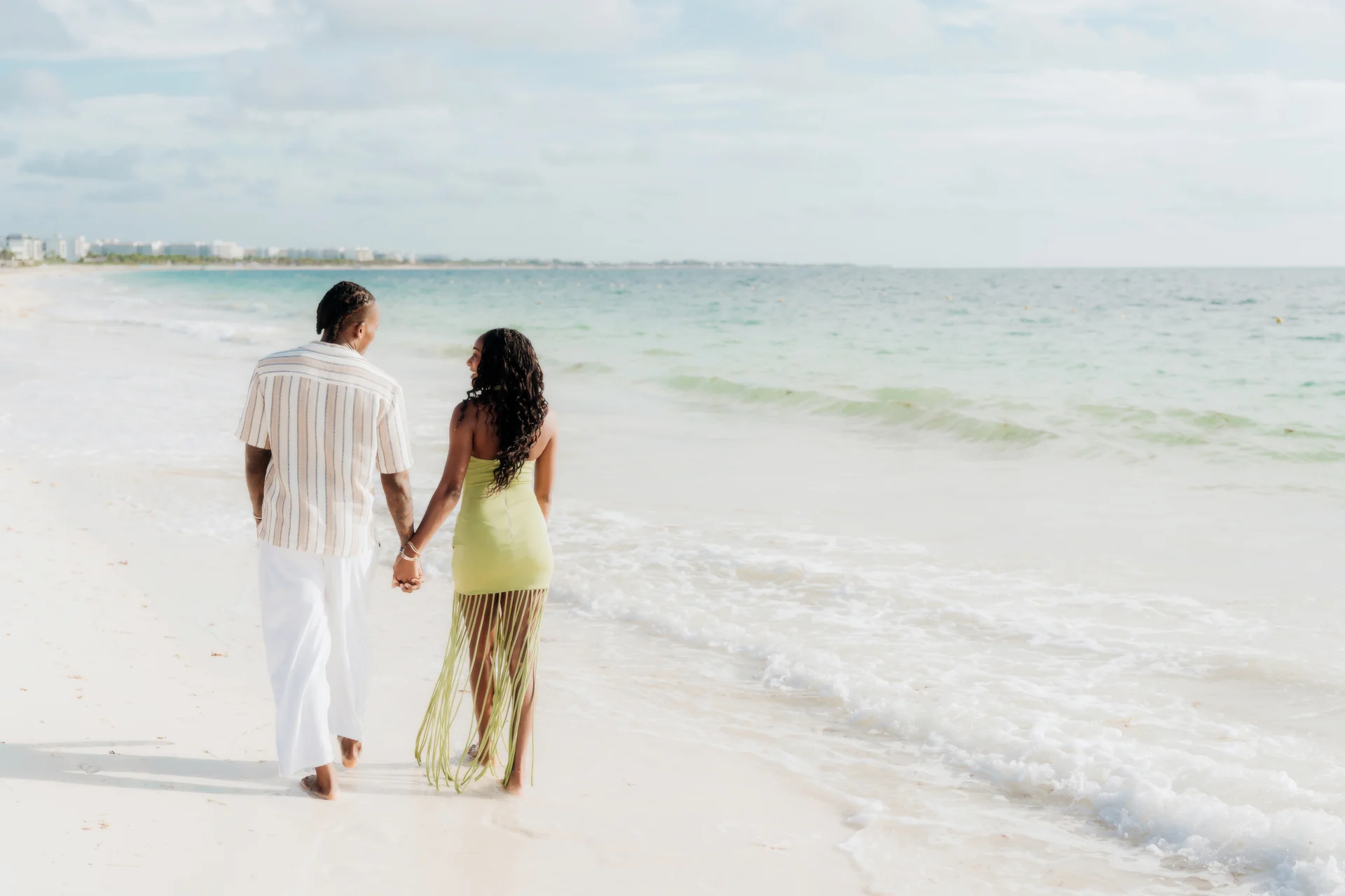 Couple seen from behind holding hands as they walk the beach beside gentle waves, RIU Latino, Costa Mujeres