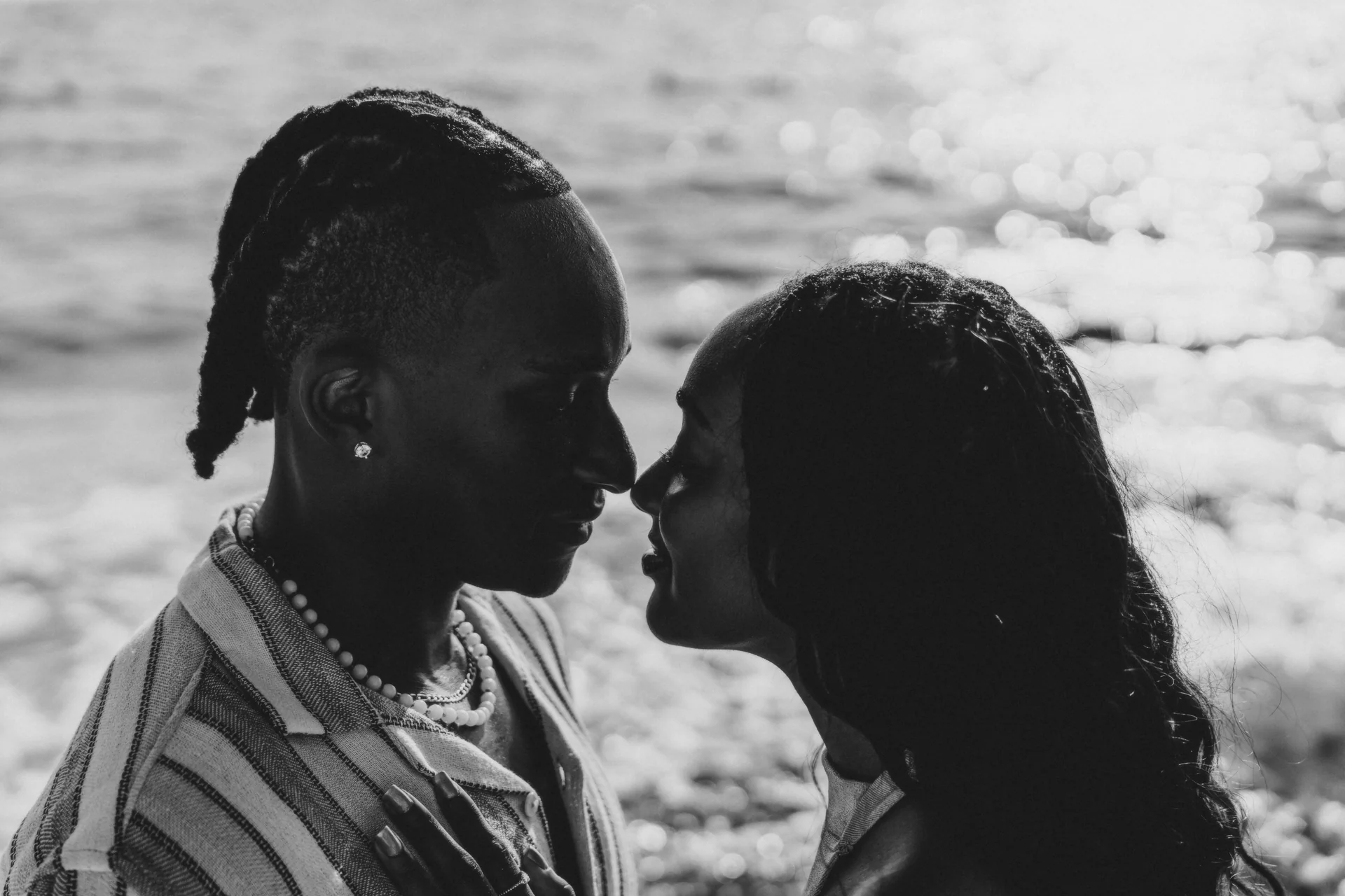 Black-and-white close profile of a couple leaning in nose to nose with sunlit water behind, RIU Latino, Costa Mujeres