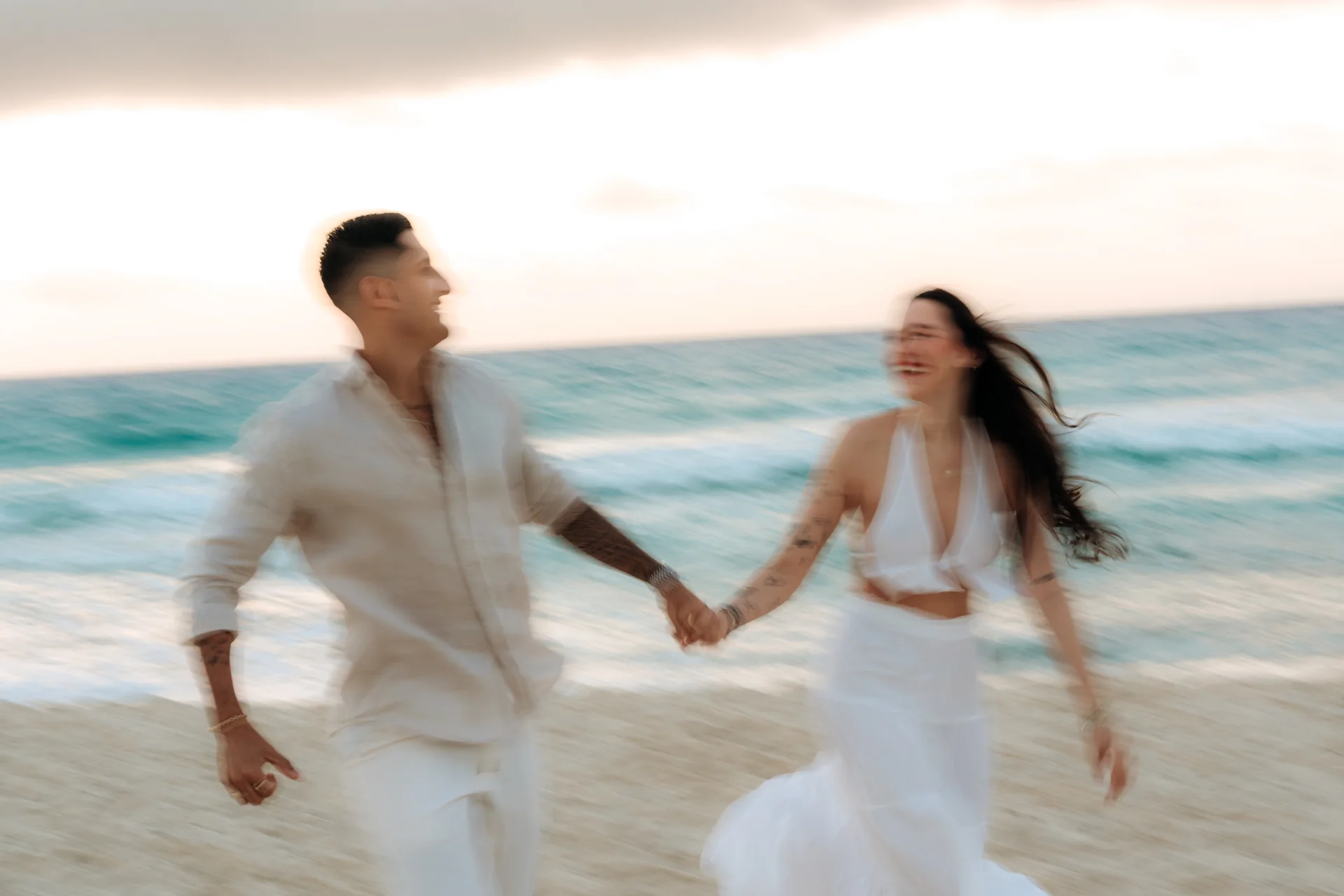 Motion-blur of a couple laughing and running hand in hand along the beach at dawn, Playa Delfines, Cancún
