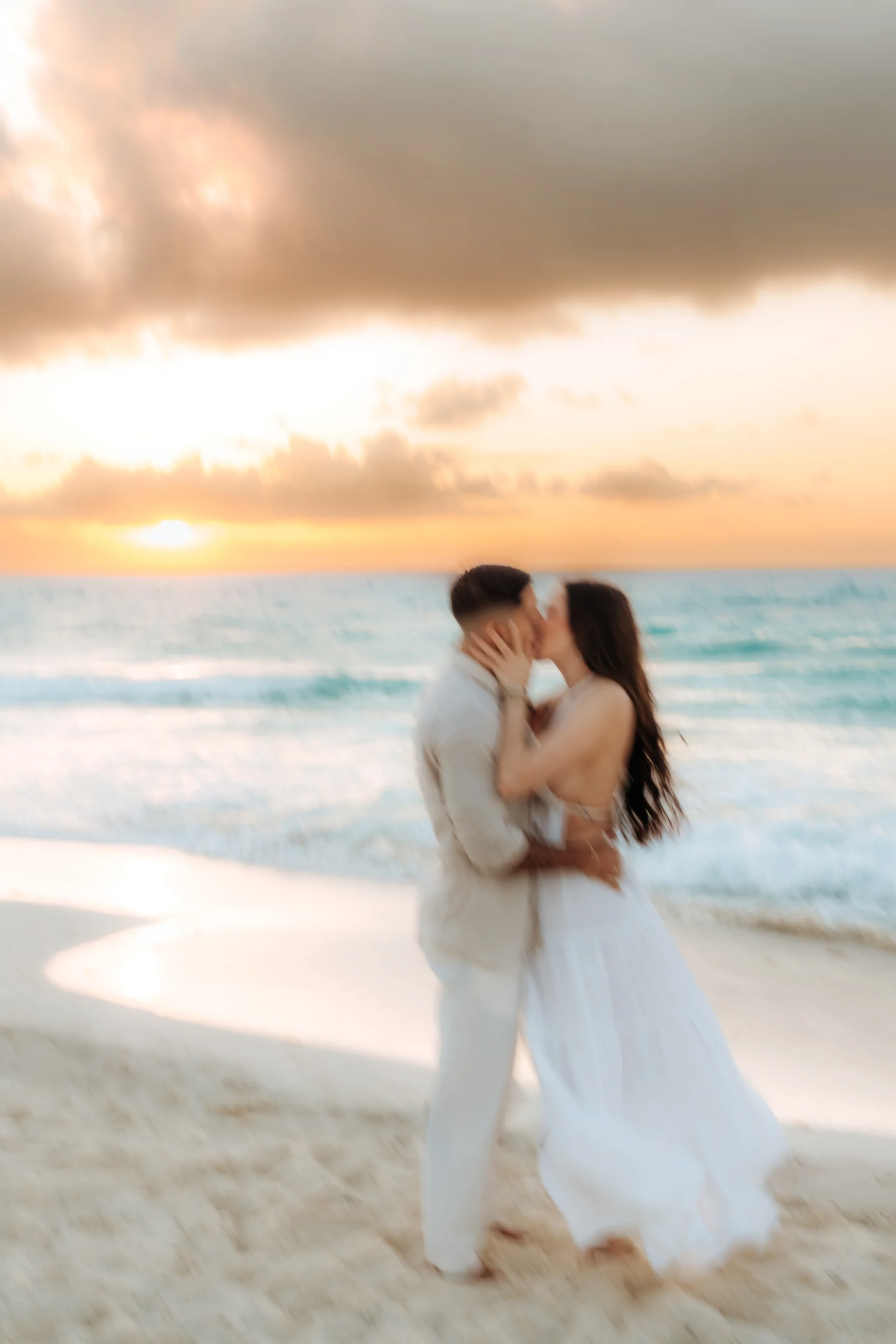 Dreamy soft-focus of a couple kissing on the sand as the sun rises over the water, Playa Delfines, Cancún
