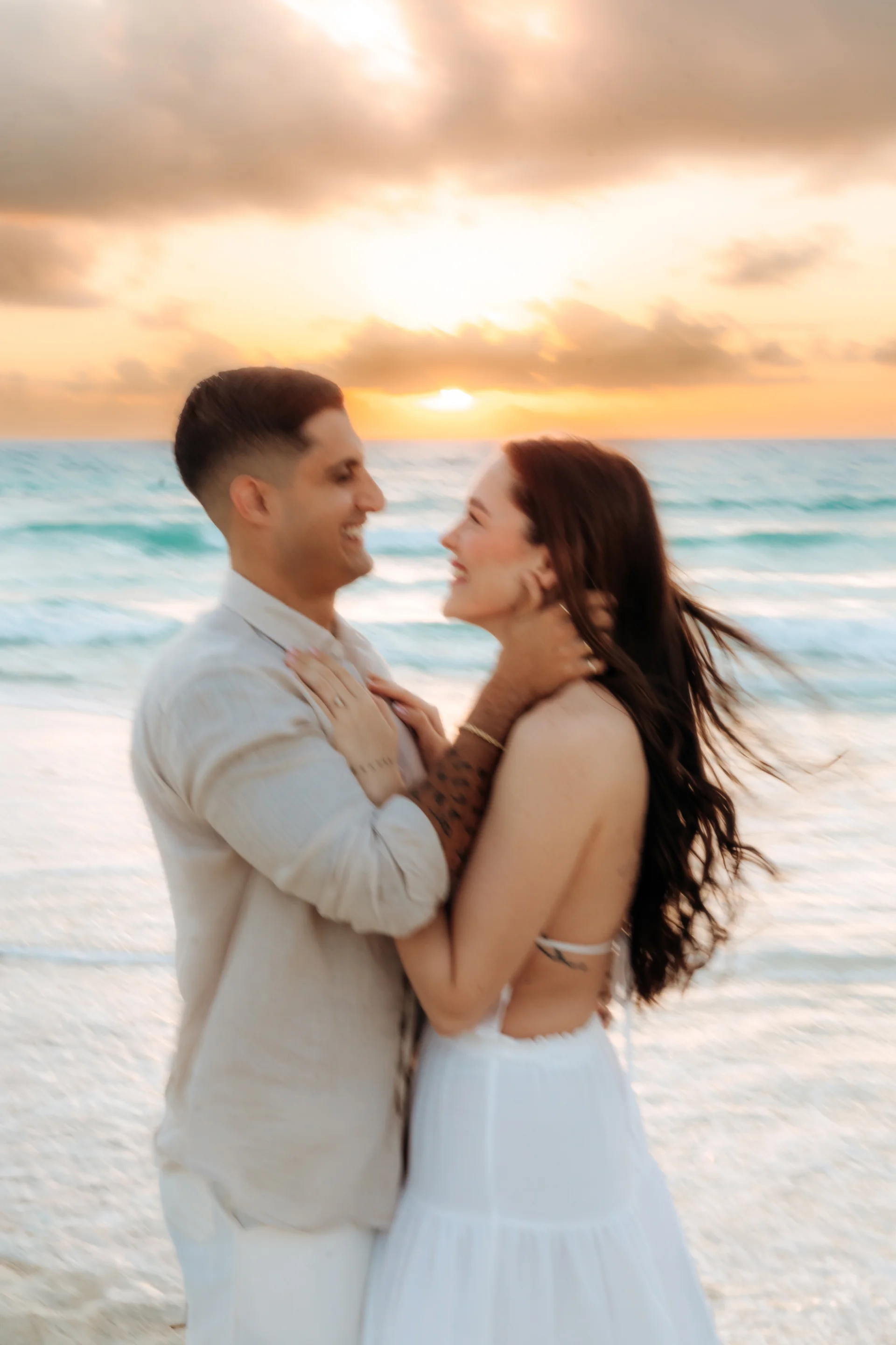 Couple embracing and smiling at each other with a golden sunrise behind them, Playa Delfines, Cancún
