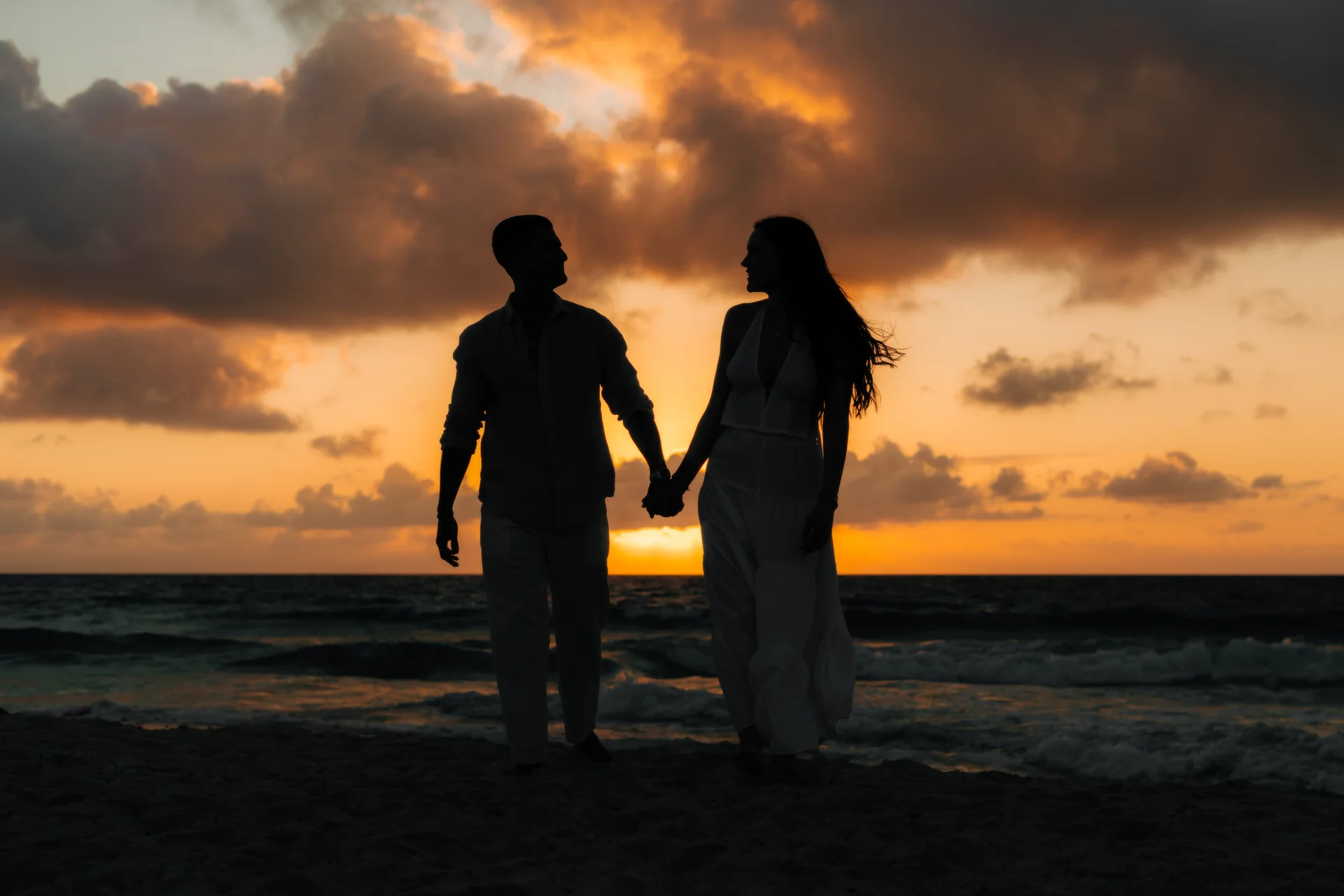 Silhouette of a couple holding hands facing each other against a vivid sunrise over the ocean, Playa Delfines, Cancún
