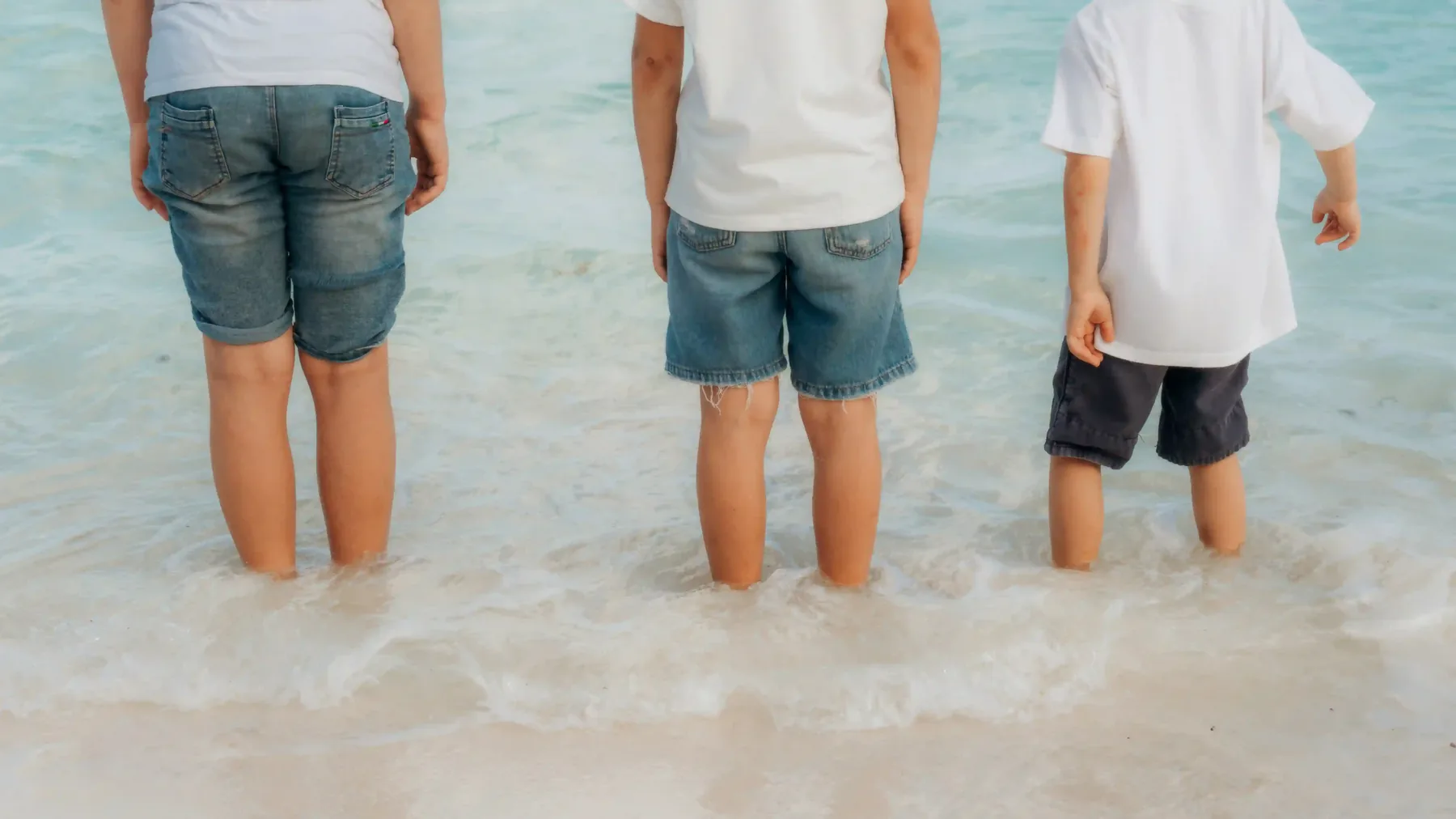 Three children at water's edge during family photo session on Cancún shoreline