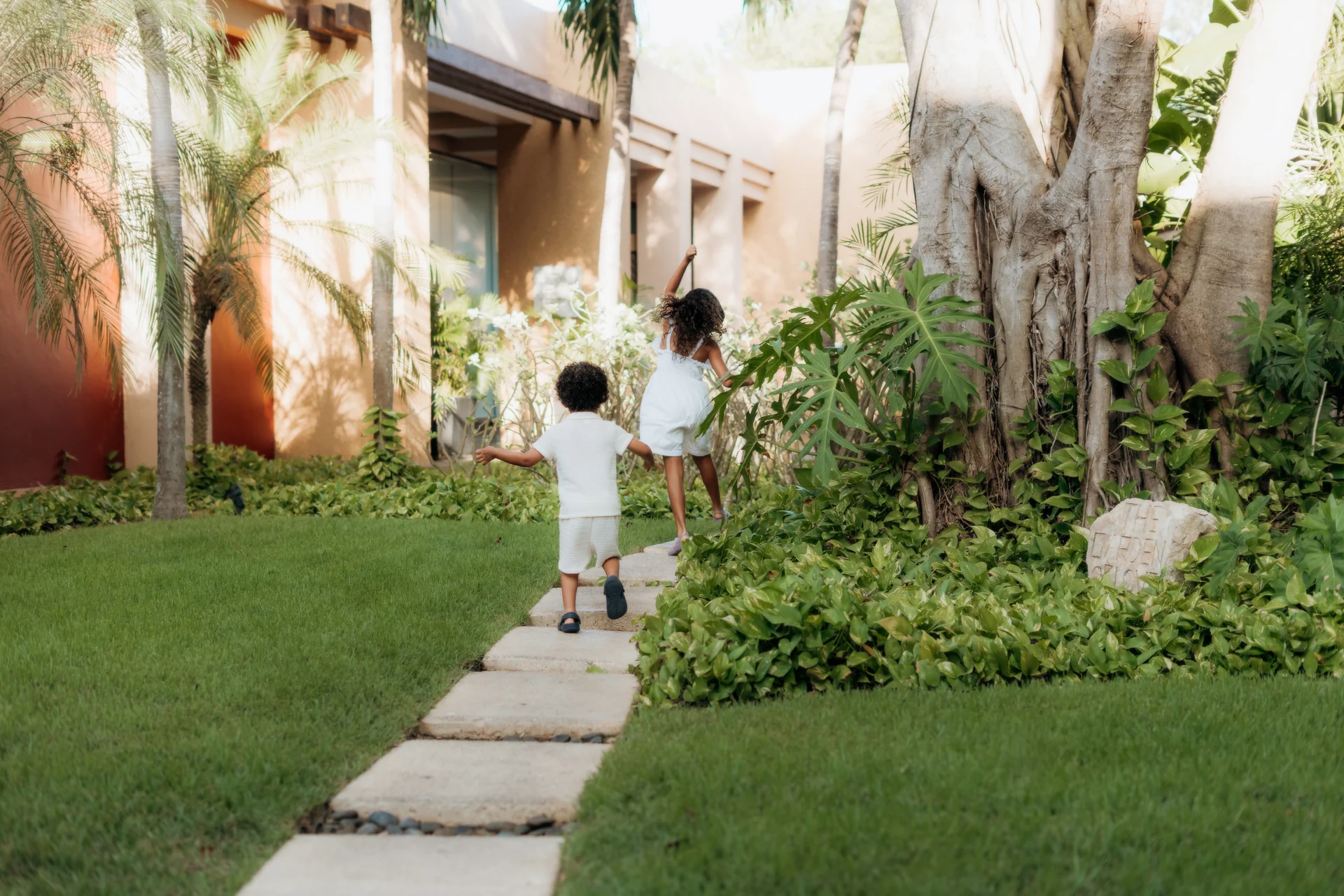 Two young children running along a stone garden path past palms and a large tree, Banyan Tree Mayakoba, Riviera Maya