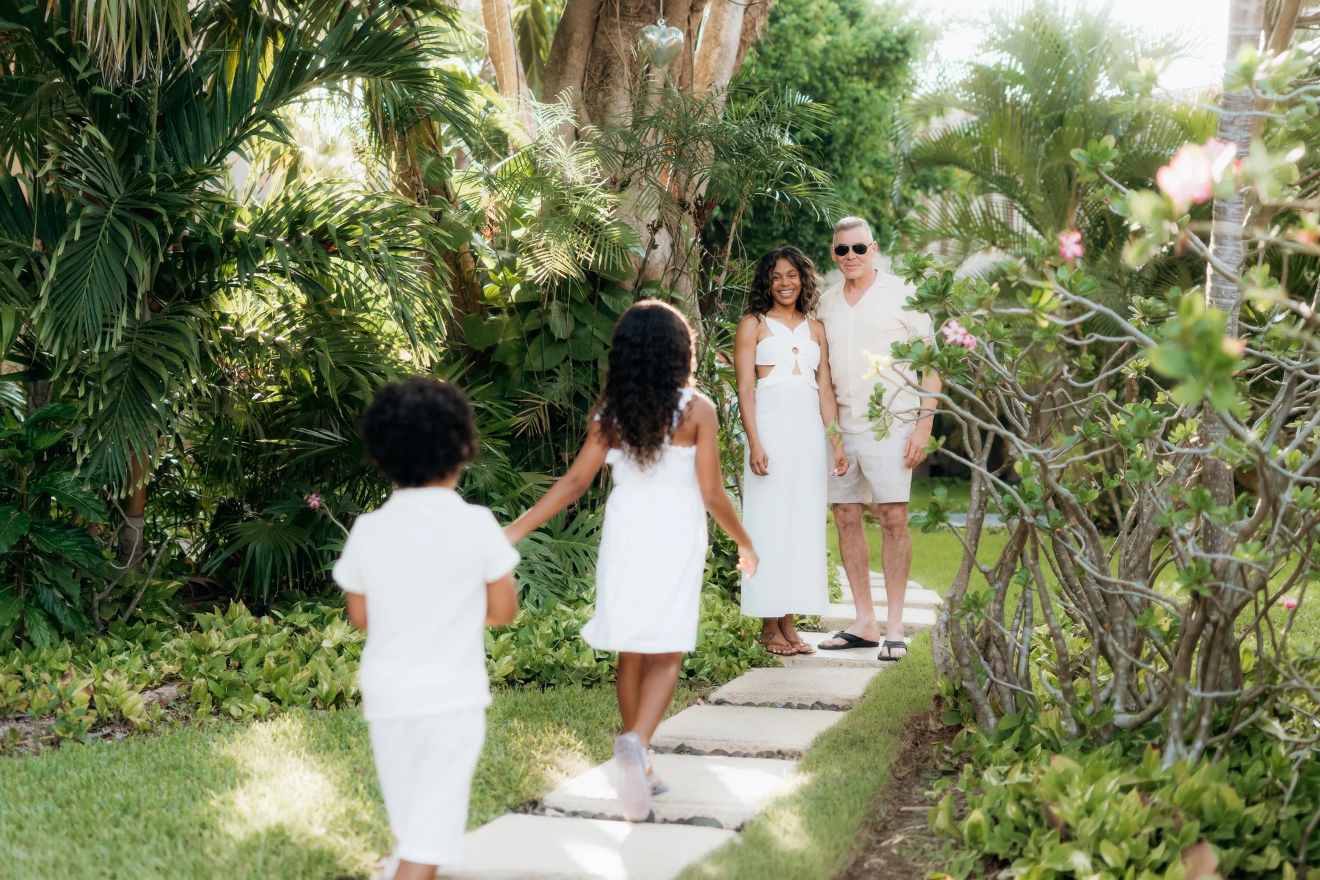 Children in white walking a garden path toward their parents through lush greenery, Banyan Tree Mayakoba, Riviera Maya