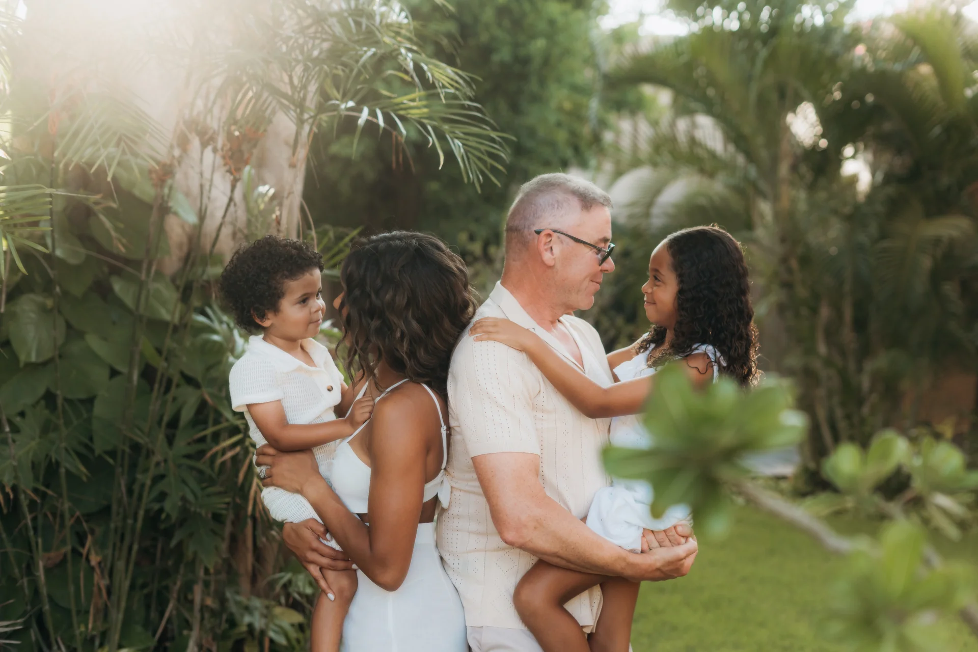 Parents holding their son and daughter face to face in the tropical resort garden at golden hour, Banyan Tree Mayakoba, Riviera Maya
