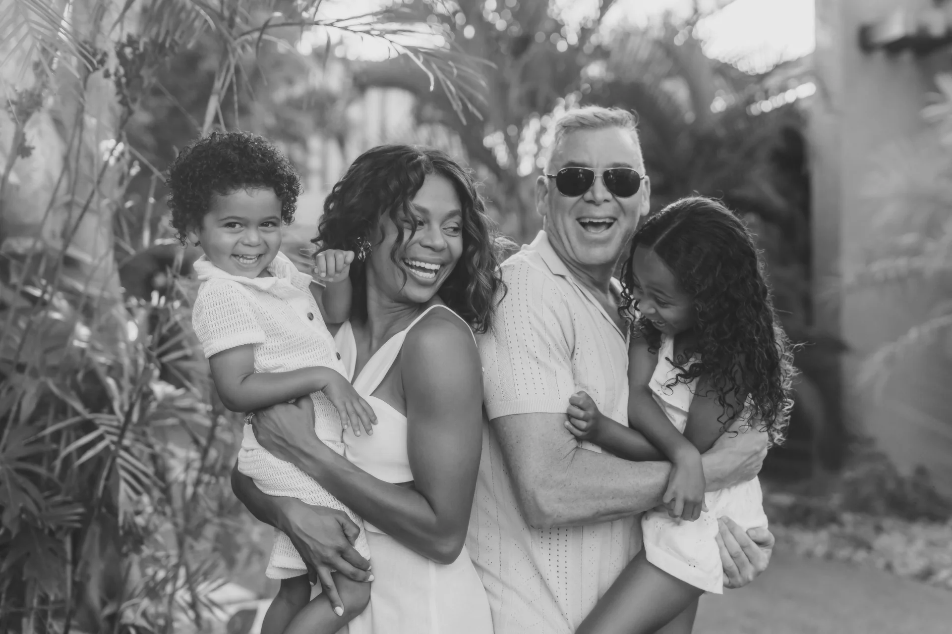 Black-and-white portrait of a smiling family of four holding their two children in the garden, Banyan Tree Mayakoba, Riviera Maya