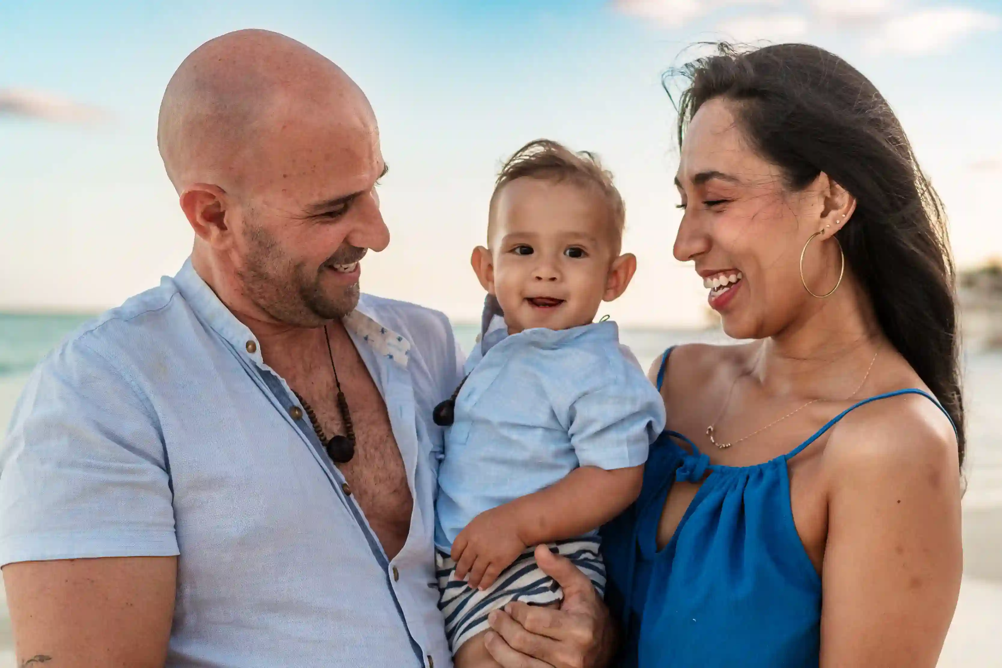 Parents with baby during family photo session on Cancun beach at sunset, parents laughing together