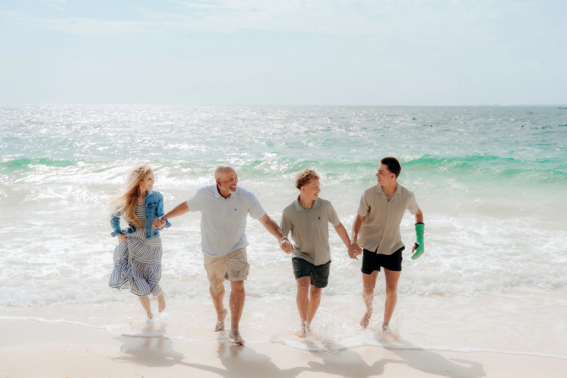 Family of four walking hand in hand through the shallow water on a Costa Mujeres beach in Cancún.