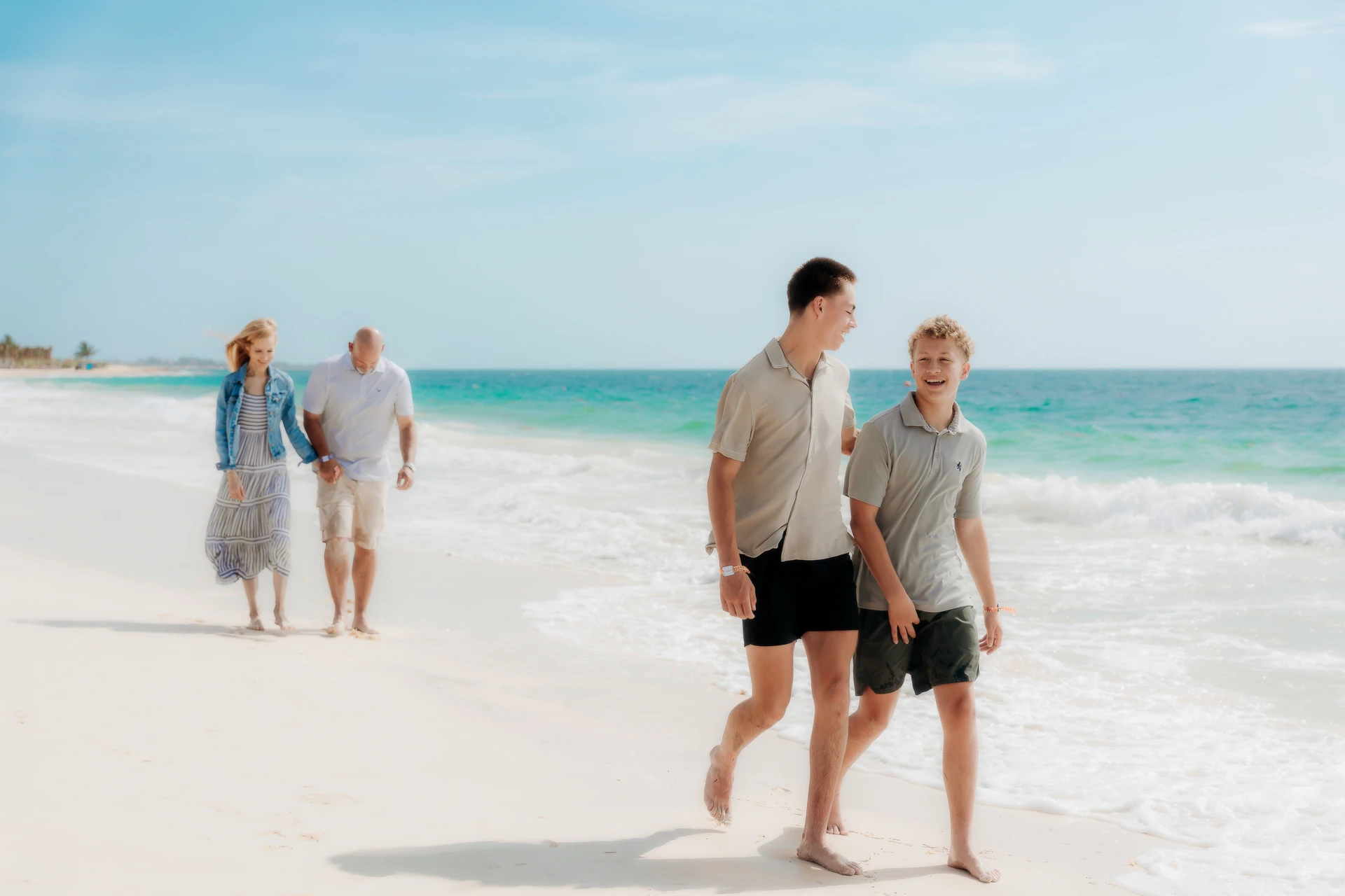 Two brothers walking ahead of their parents along the turquoise Cancún shoreline.