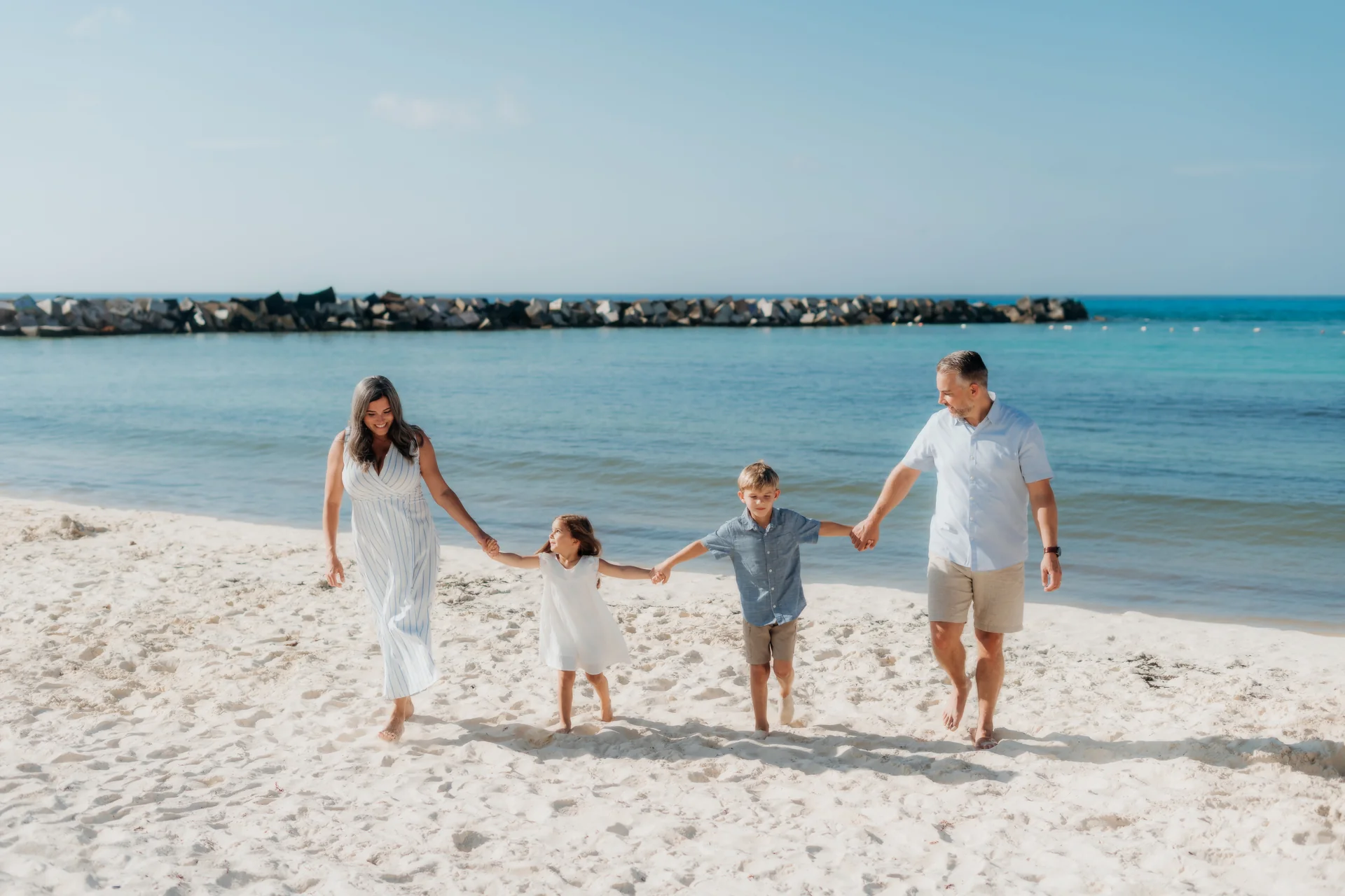 Family of four walking hand in hand along Forum Beach, Hyatt Ziva, Cancún