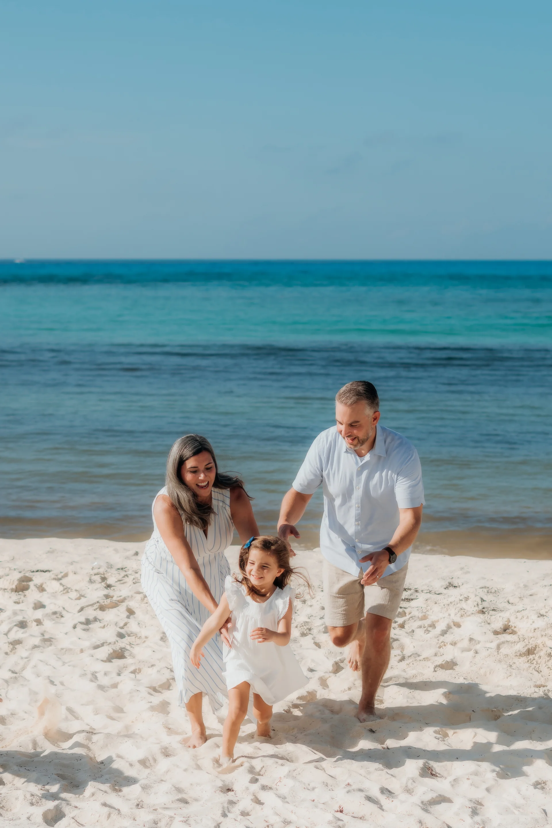 Family of four walking on the sand beside turquoise water, parents guiding their young daughter, Hyatt Ziva, Cancún