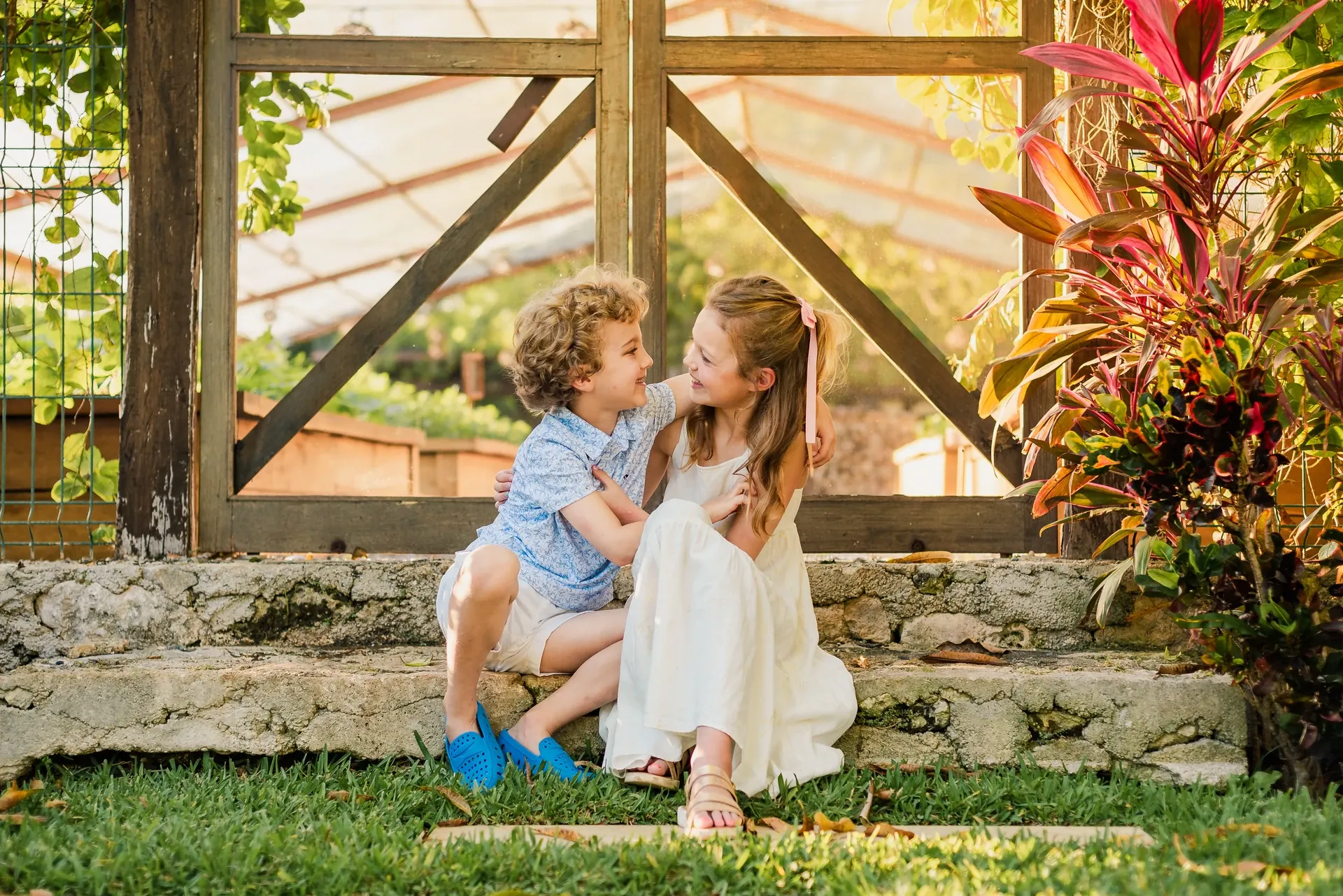 A young brother and sister sitting together on stone steps in the gardens at Rosewood Mayakoba.