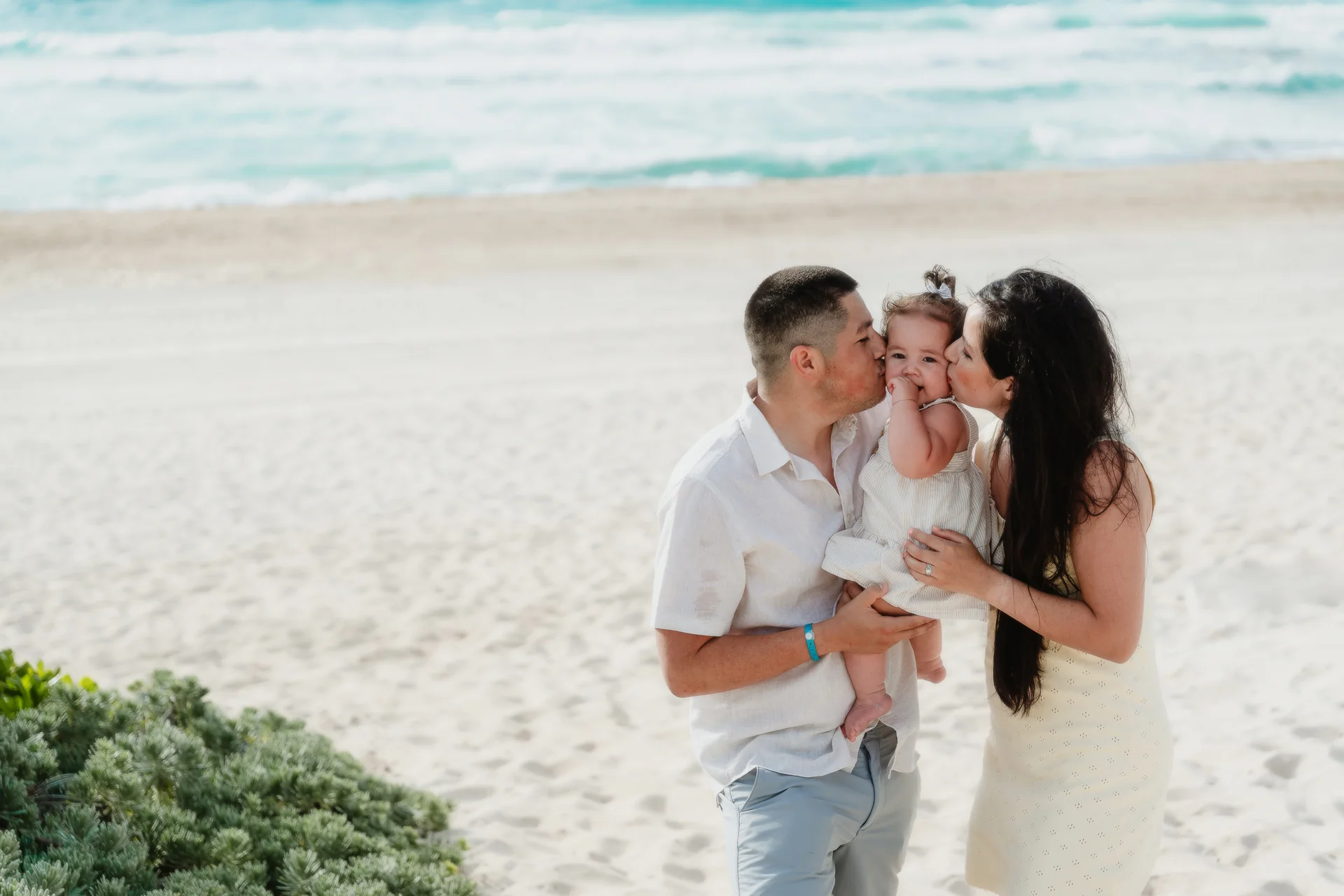 Parents kissing their baby daughter on both cheeks on the beach, Playa Delfines, Cancún