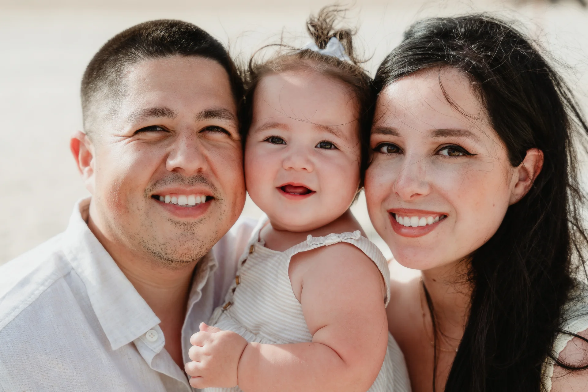 Close family portrait of parents cheek to cheek with their baby daughter, Playa Delfines, Cancún