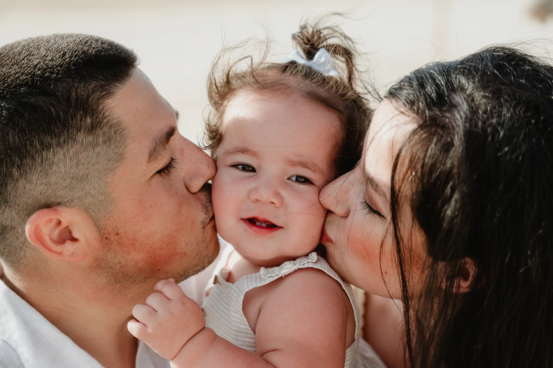 Parents kissing their smiling baby daughter on both cheeks, Playa Delfines, Cancún
