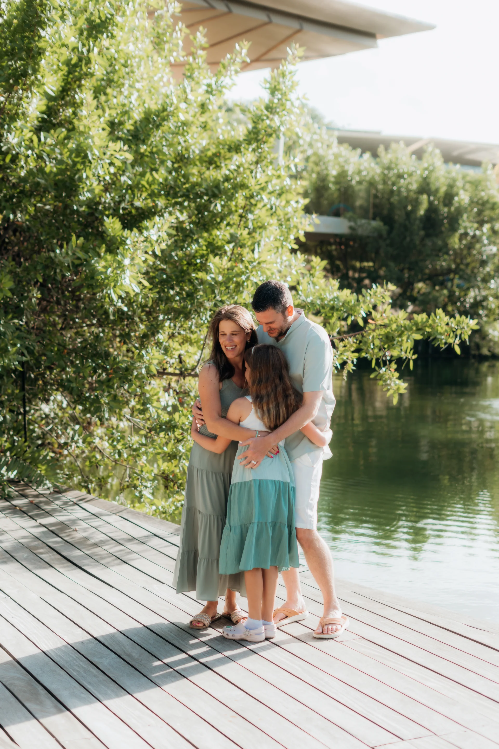 Family of three sharing a group hug on a wooden dock beside the lagoon and mangroves, Rosewood Mayakoba, Riviera Maya