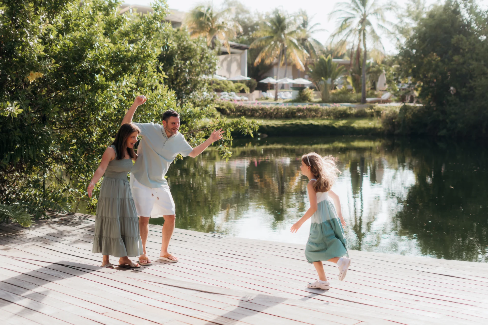 Young daughter running toward her cheering parents on a lagoon-side wooden deck, Rosewood Mayakoba, Riviera Maya