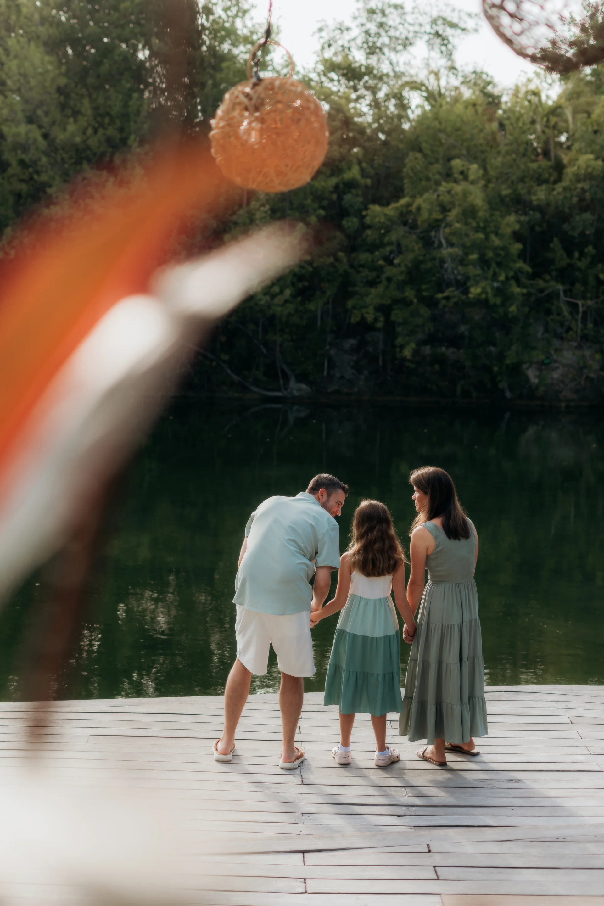 Family of three standing together on a dock looking out over the still green lagoon, Rosewood Mayakoba, Riviera Maya