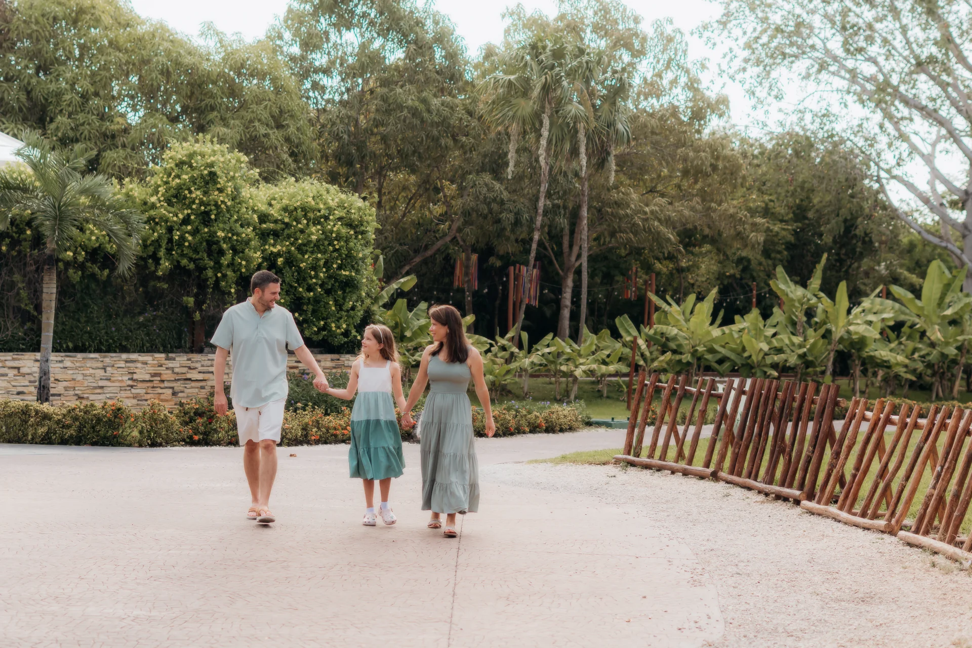 Family of three holding hands walking along a garden path lined with tropical greenery, Rosewood Mayakoba, Riviera Maya