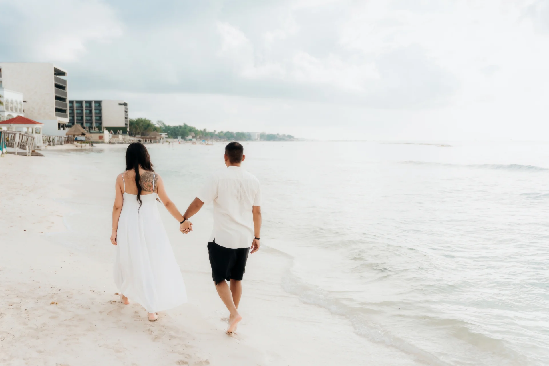 Couple walking hand in hand along the shoreline with the resort behind them, Hyatt Vivid, Playa del Carmen