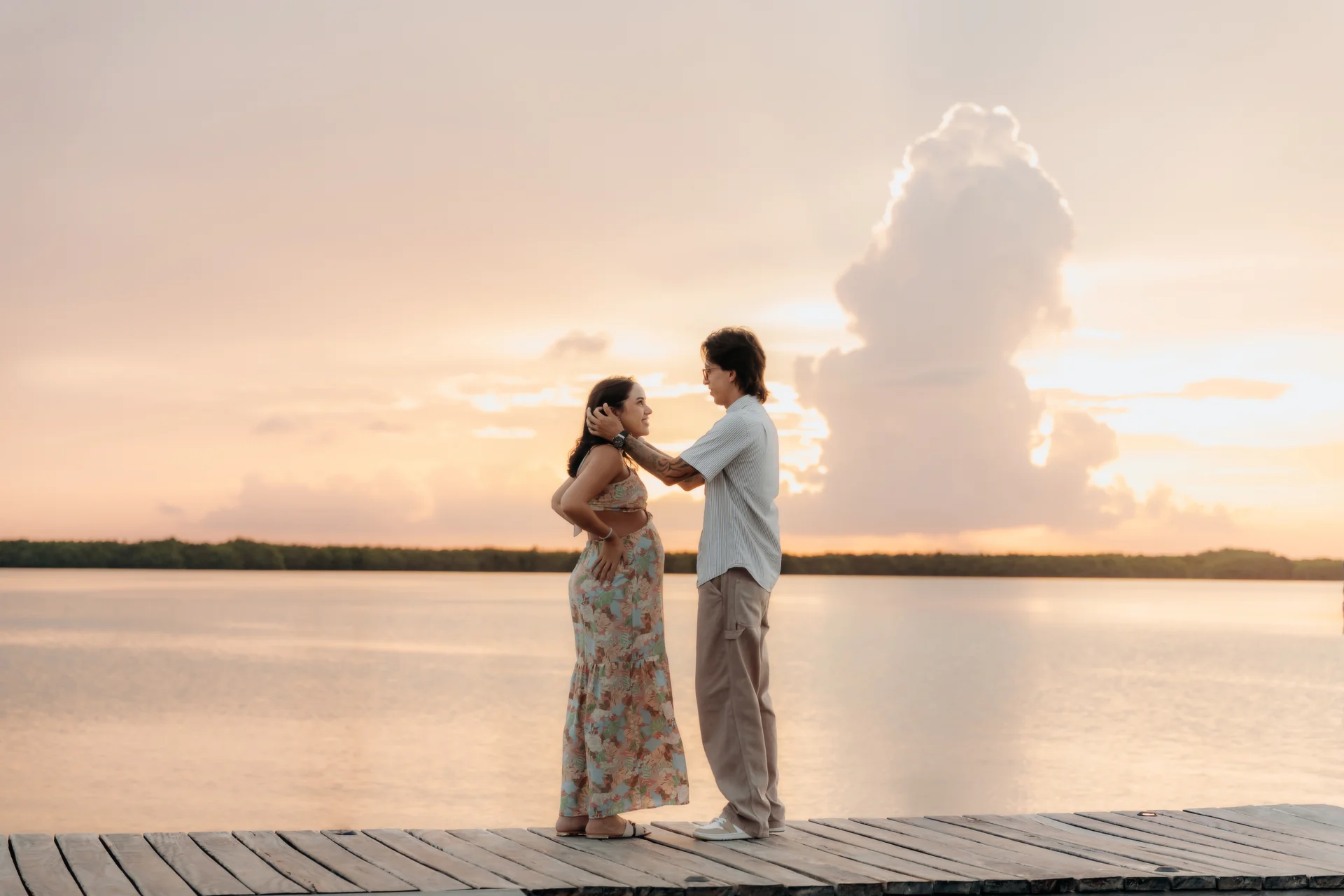 Expecting couple facing each other on the dock as the sun sets over the lagoon, Navios restaurant, Cancún