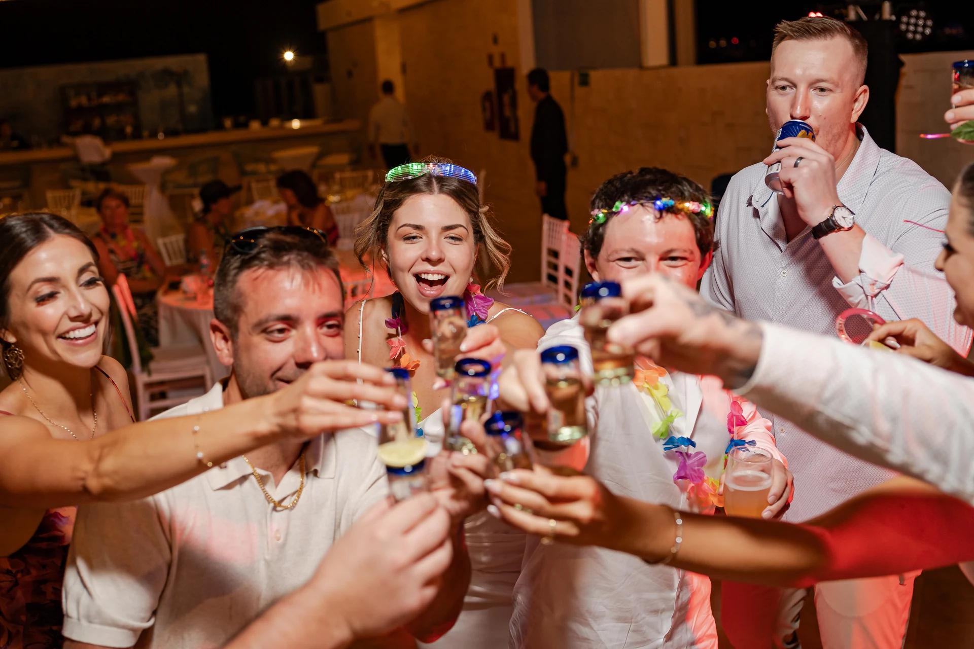 Wedding guests raising shot glasses together in a circle on the dance floor at night