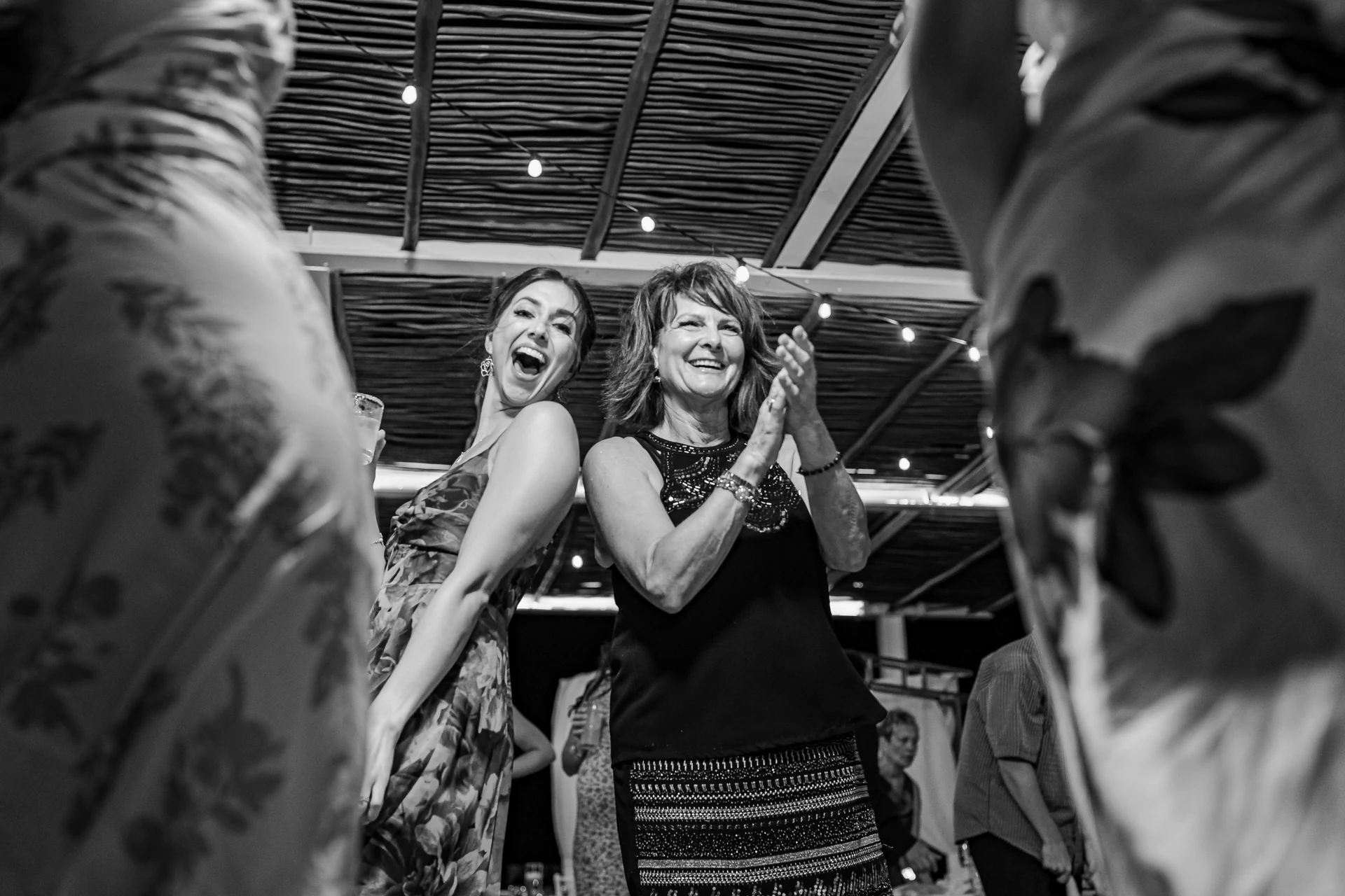 Black and white photograph of wedding guests laughing and clapping under string lights on the dance floor