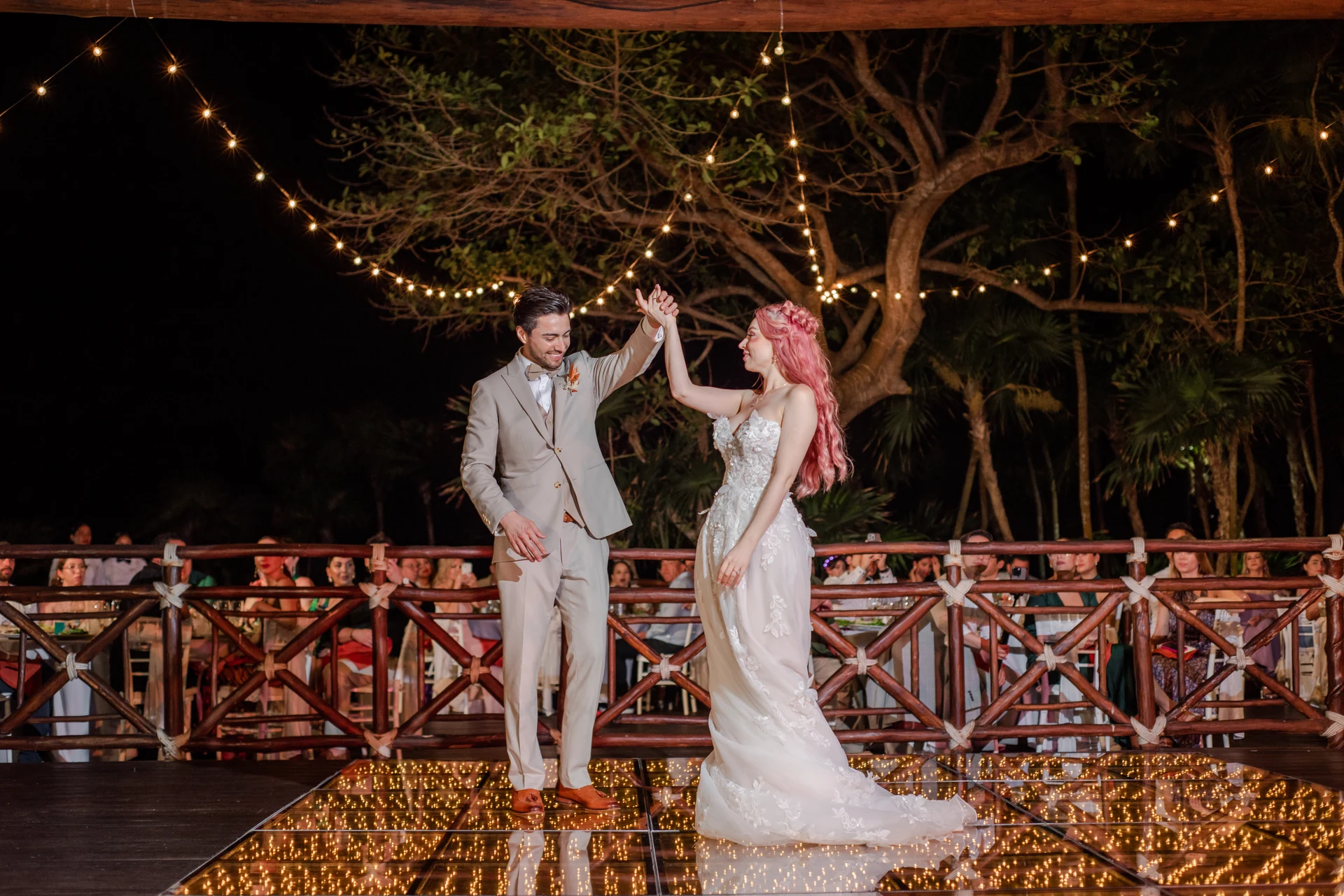 Bride and groom sharing their first dance at night under a tree lit with warm string lights