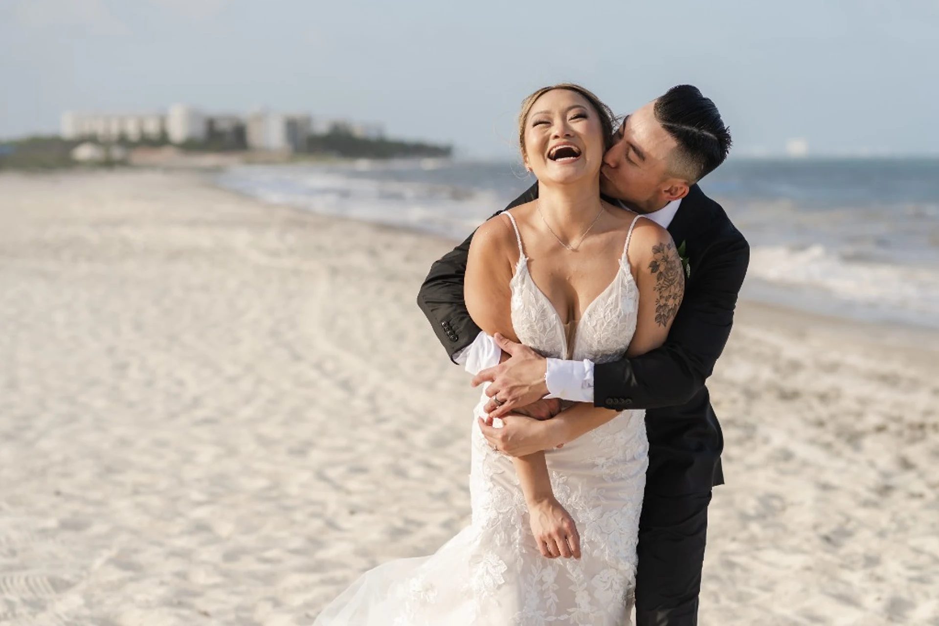 Groom embracing the laughing bride from behind on the beach