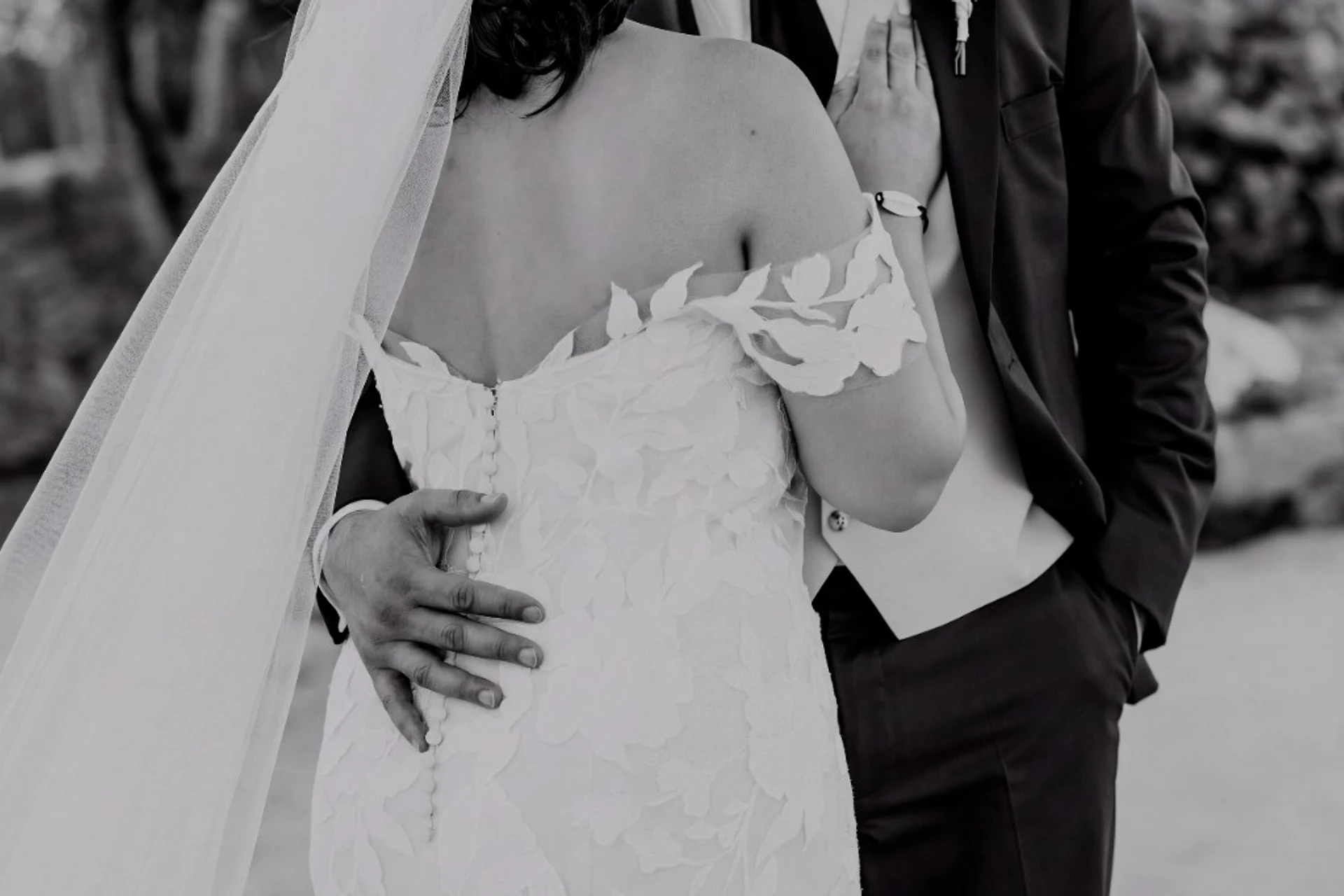 Black and white close-up of the groom's hand resting on the back of the bride's lace dress and her hand on his lapel